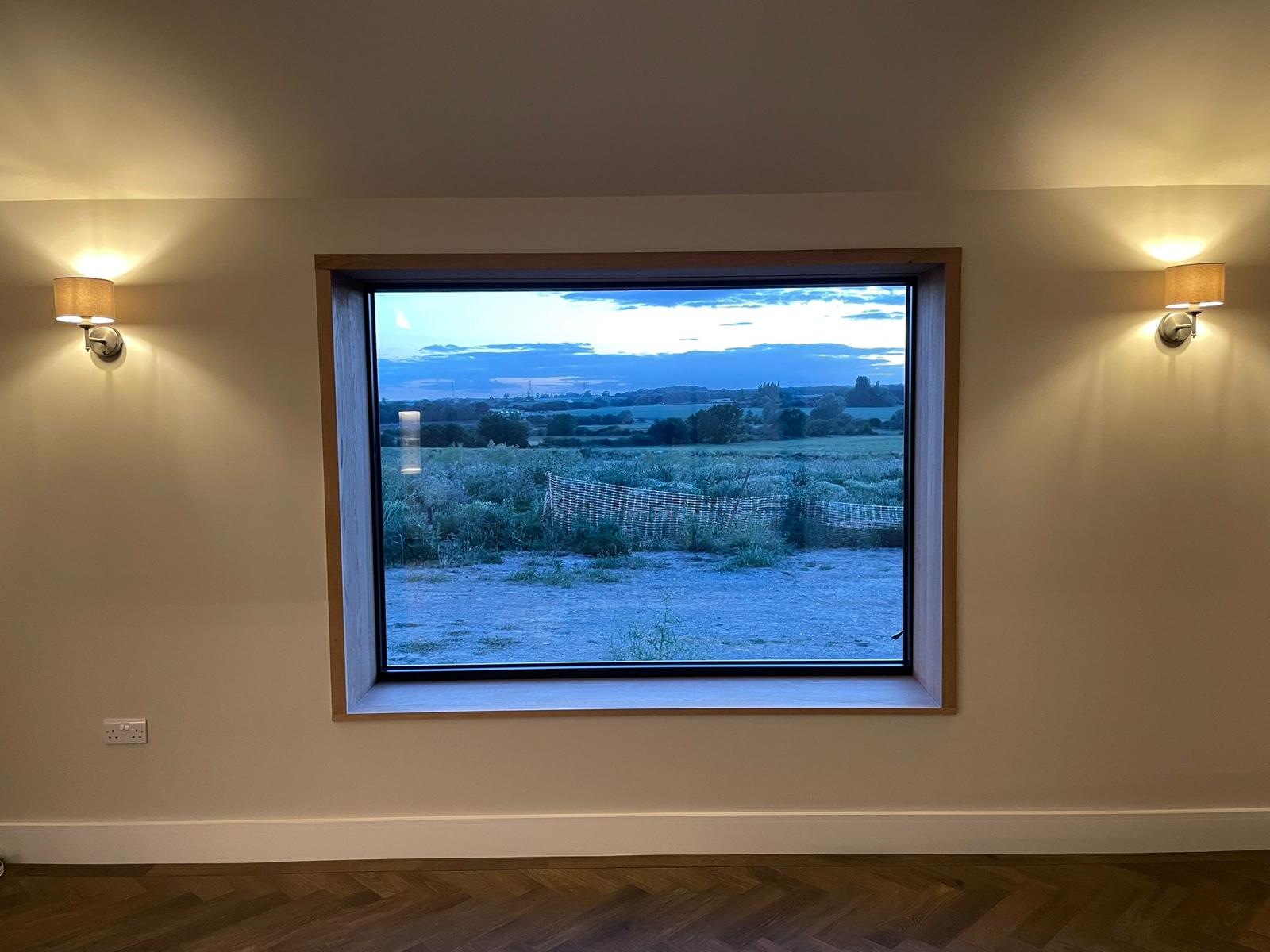 Large picture window with a countryside view, wall lights and wooden flooring